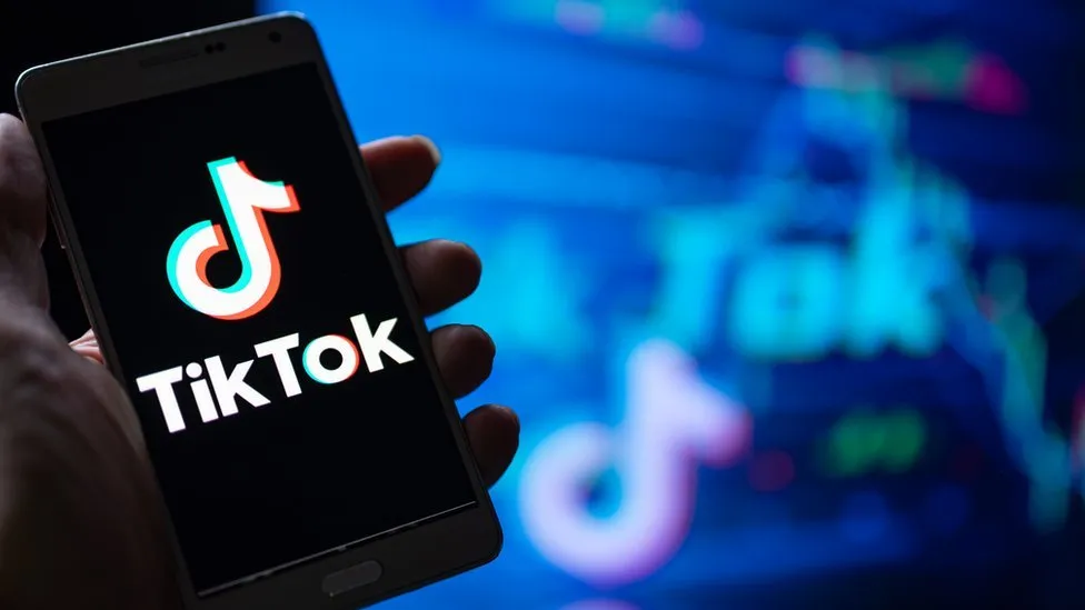 Mano sosteniendo smartphone con logo TikTok y logotipos desenfocados en el fondo