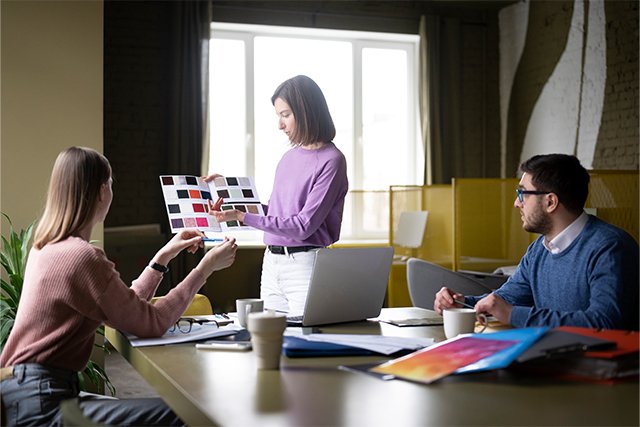 Una agencia de marketing discute ideas creativas para una campaña visual. La responsable del proyecto presenta una paleta de colores y muestras de diseño mientras recibe comentarios del equipo