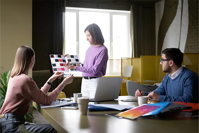 Una agencia de marketing discute ideas creativas para una campaña visual. La responsable del proyecto presenta una paleta de colores y muestras de diseño mientras recibe comentarios del equipo