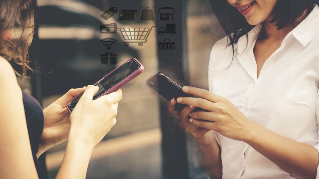 Dos mujeres usando sus teléfonos móviles con íconos de comercio electrónico sobrepuestos.