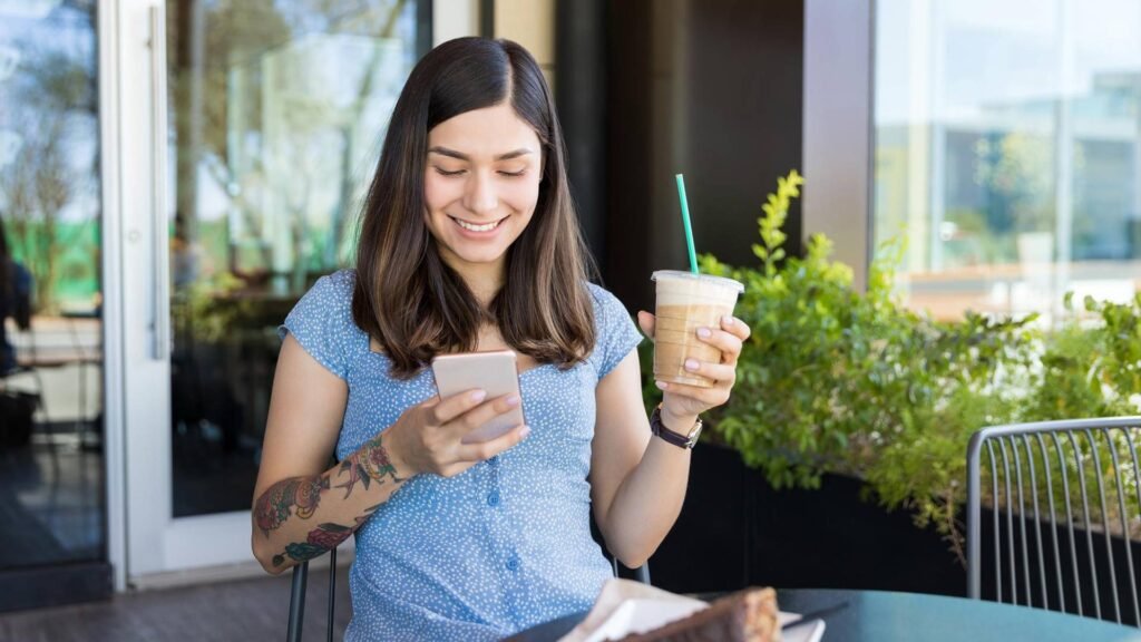 Mujer joven usando su smartphone mientras toma café en una terraza.